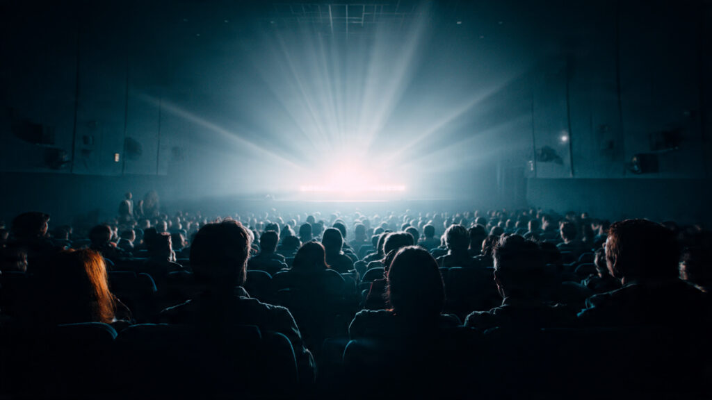 An audience captivated in a dark cinema, focused on the brightly lit screen.