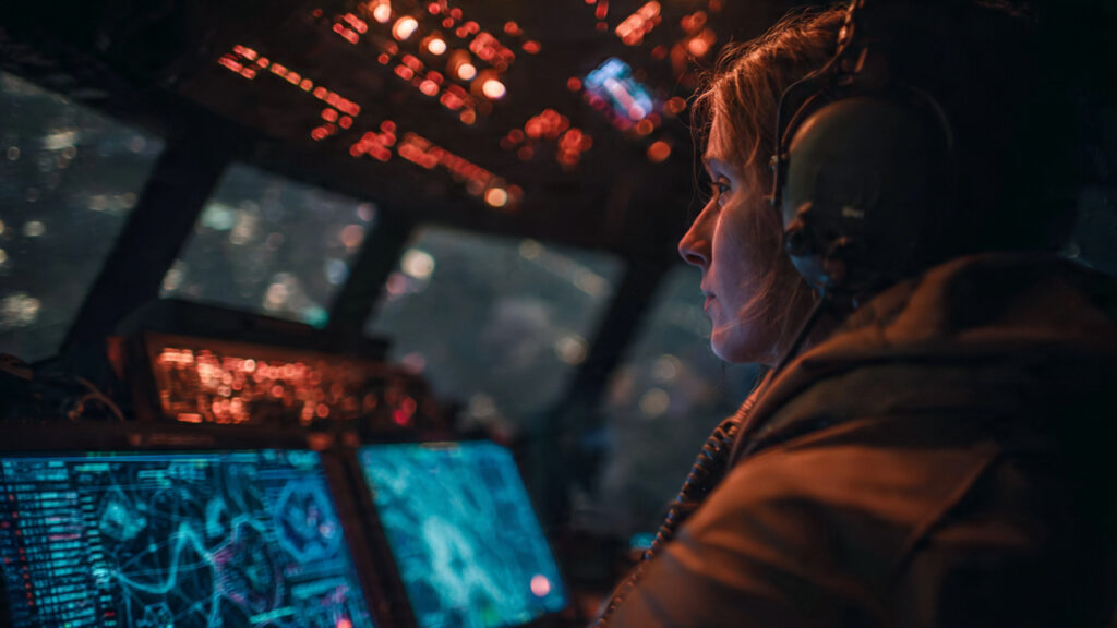 A futuristic drone pilot's POV in a dimly lit control room, with holographic displays showing battlefield data