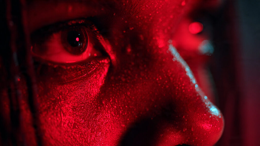 Close-up of a character's face bathed in intense red neon light