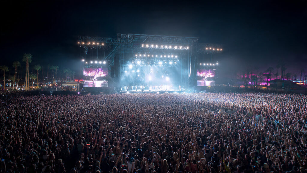 Sabrina Carpenter's "Sabrinawood" Takes Over Coachella 2026: A Night of Vintage Glamour and Surprise Cameos 4 Wide shot of the Coachella crowd illuminated by stage lights, with Sabrina Carpenter as a distant figure